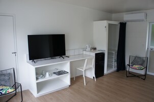 A compact kitchenette with a flat-screen TV, a white chair, and a small refrigerator.