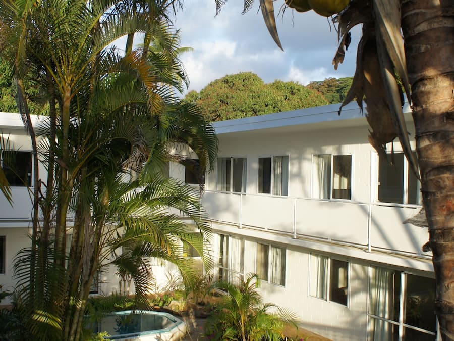A two-story building with a pool, surrounded by palm trees and a garden.