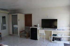 Una habitación compacta con una cama, un escritorio con computadora, televisión y microondas.