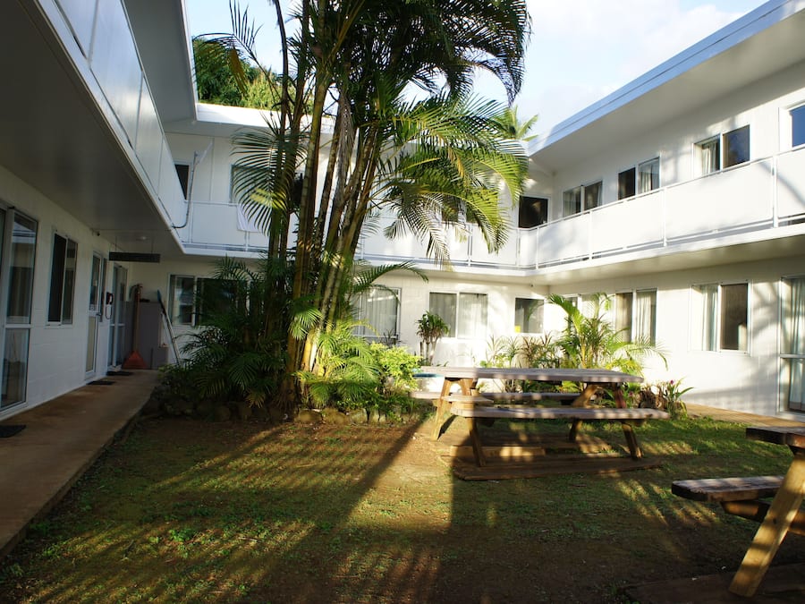 A courtyard with a wooden bench, palm trees, and a building with multiple windows and balconies.