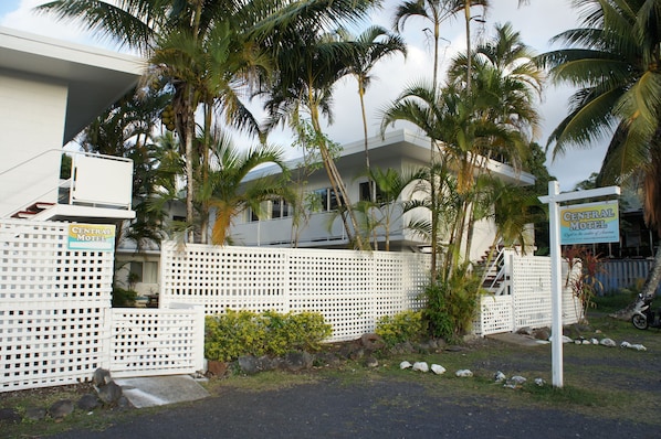 Un motel céntrico con cerca blanca, palmeras y un edificio moderno.