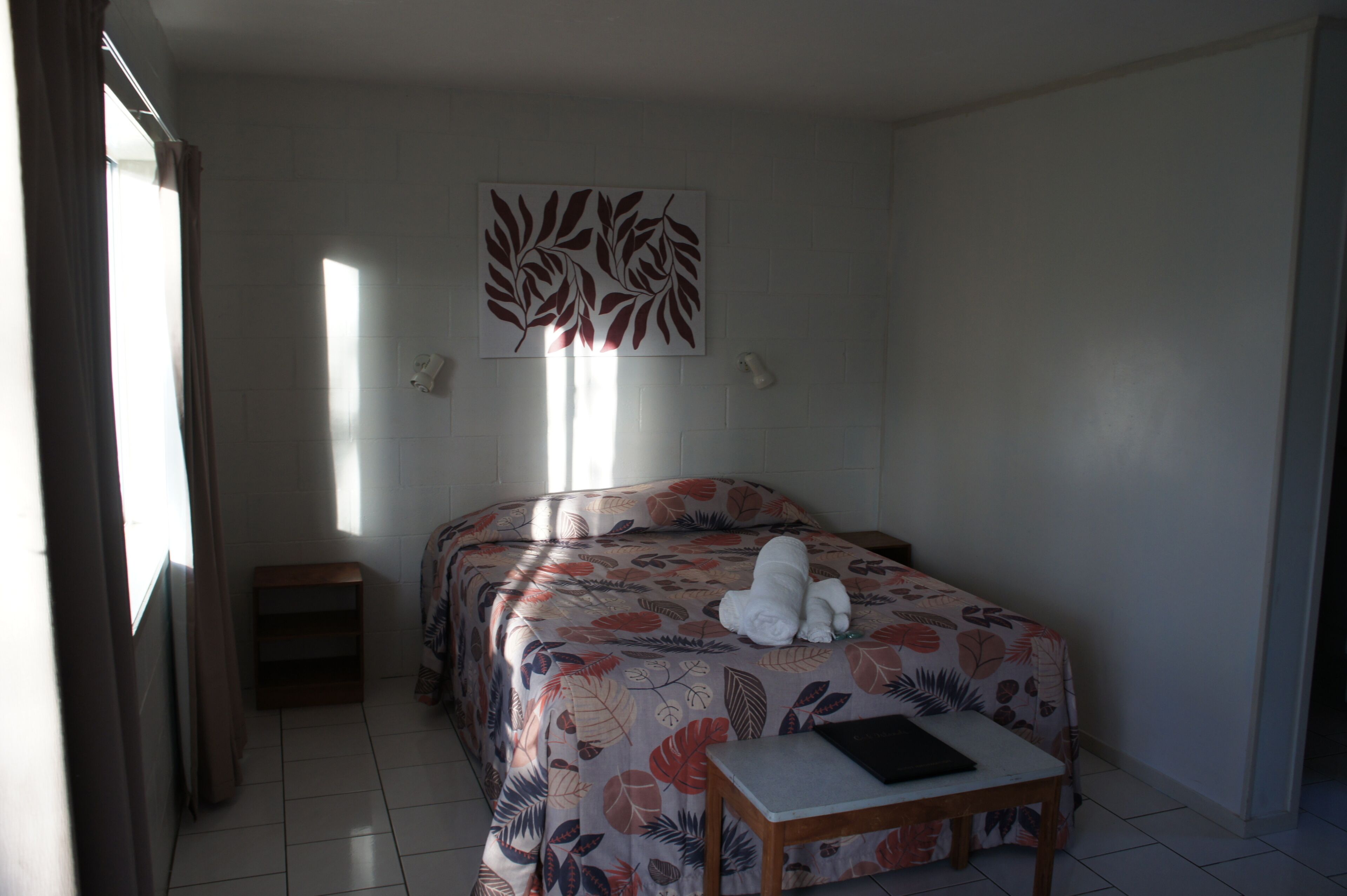 Une chambre d’hôtel avec deux lits, une petite table, un luminaire fixé au mur et une fenêtre avec des rideaux.