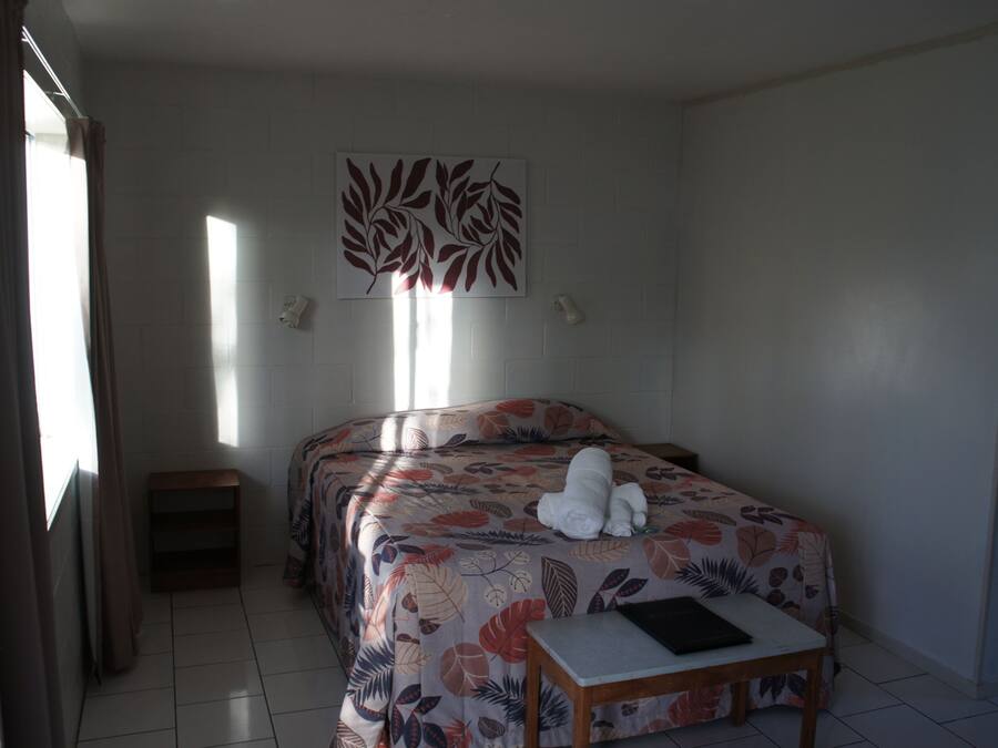 Une chambre d’hôtel avec deux lits, une petite table, un luminaire fixé au mur et une fenêtre avec des rideaux.