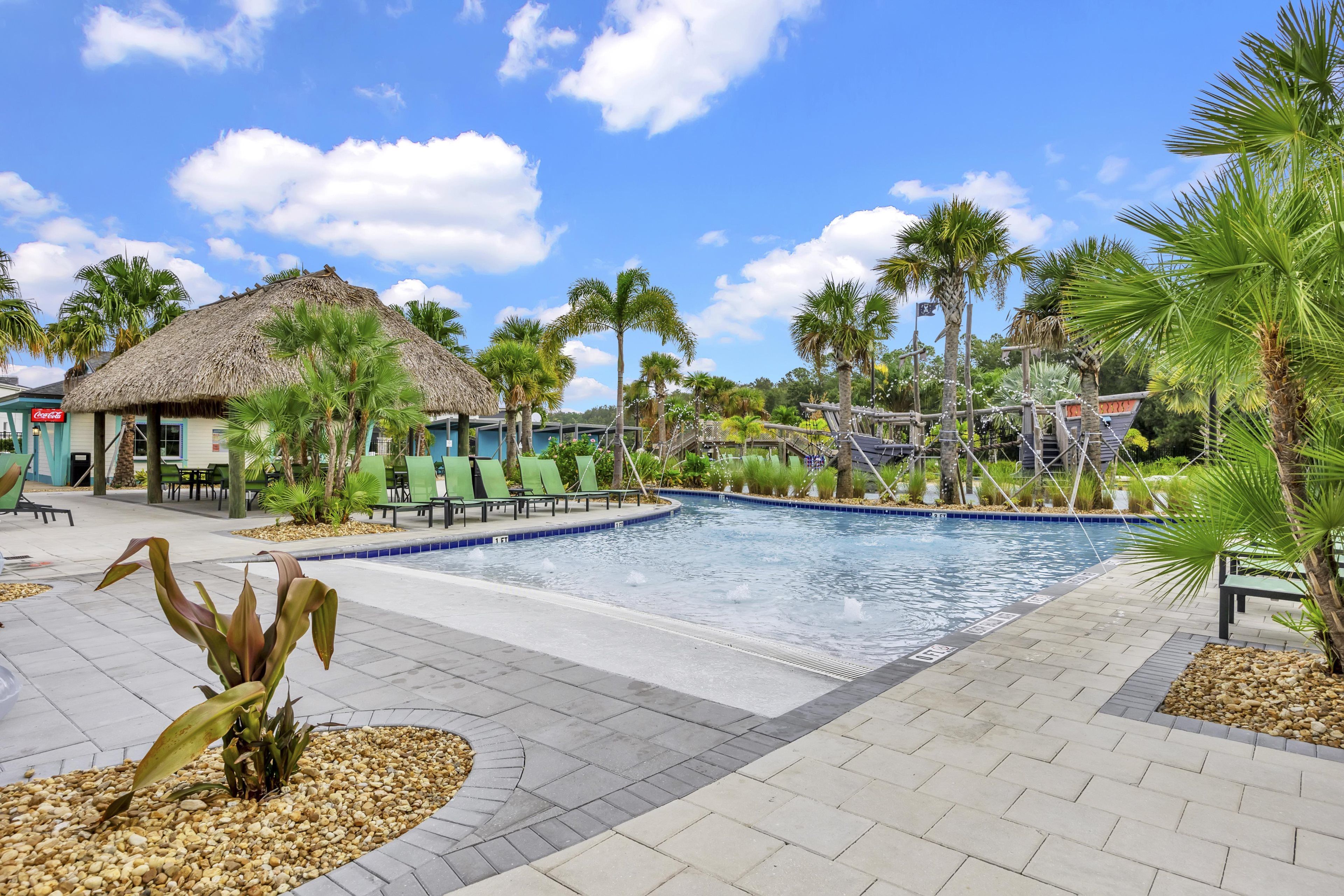 A swimming pool area with lounge chairs, palm trees, and a thatched-roof building.