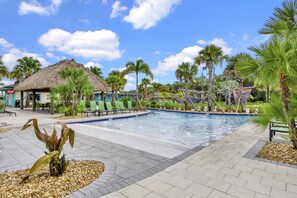 A swimming pool area with lounge chairs, palm trees, and a thatched-roof building. - Private pool, resorts, 9 minutes to Disney (Kissimmee)