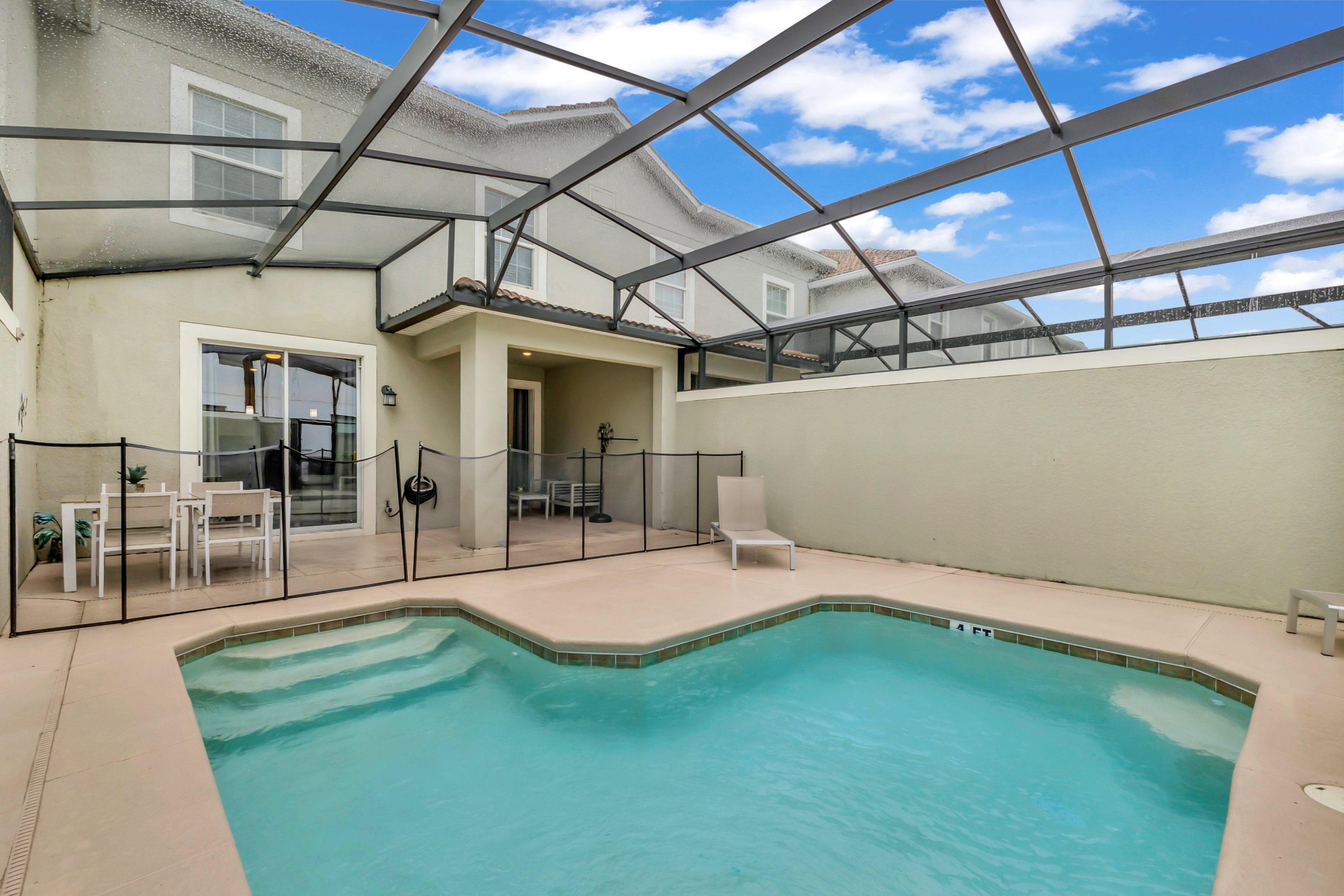 An indoor swimming pool with a glass ceiling, surrounded by a fenced area with seating and a door leading to a covered patio.