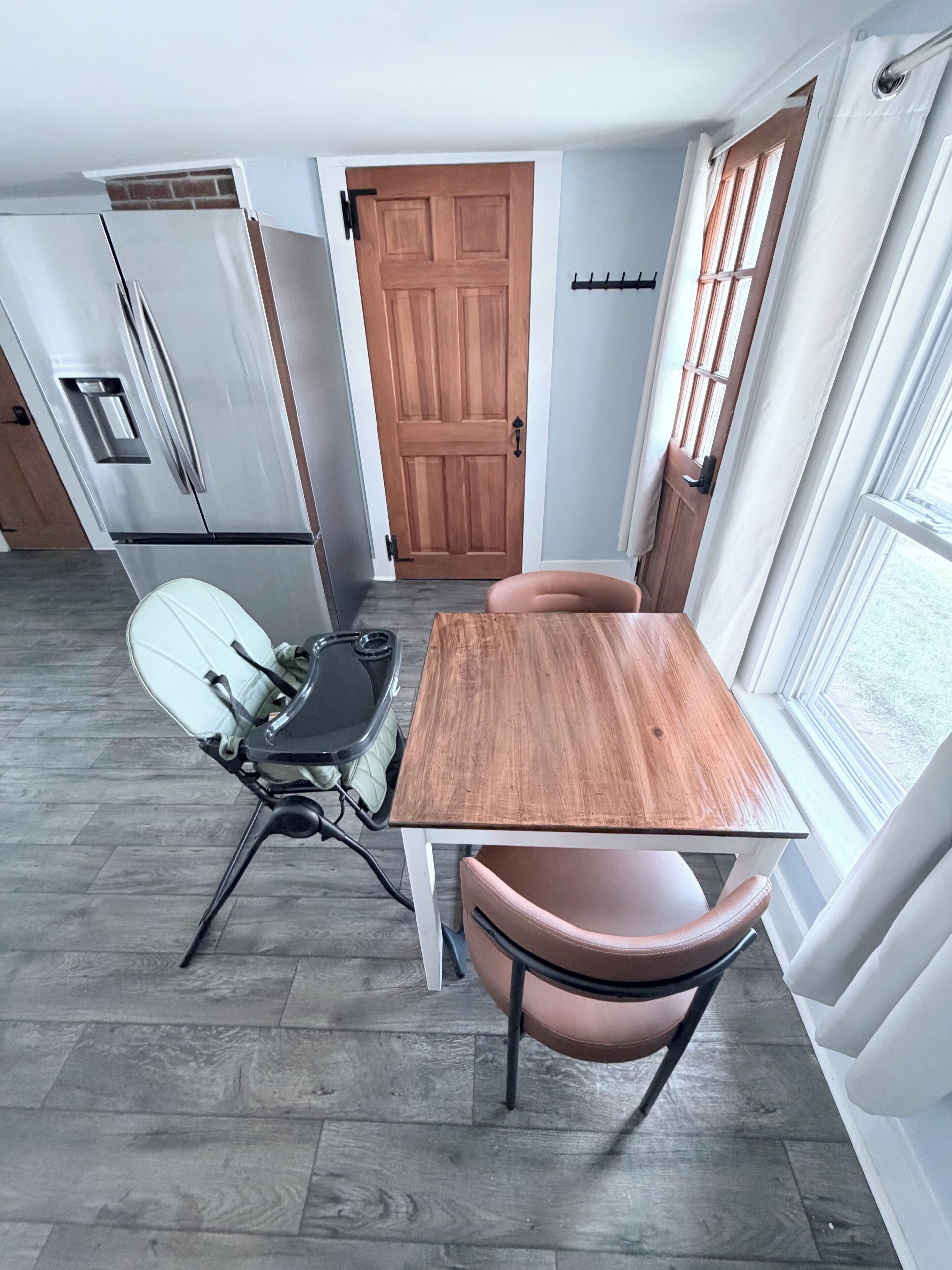 A compact kitchen with a wooden table and chairs, a built-in oven, and a refrigerator.