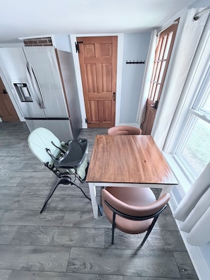 Een kleine keuken met een houten tafel en stoelen, een inbouwoven en een koelkast.