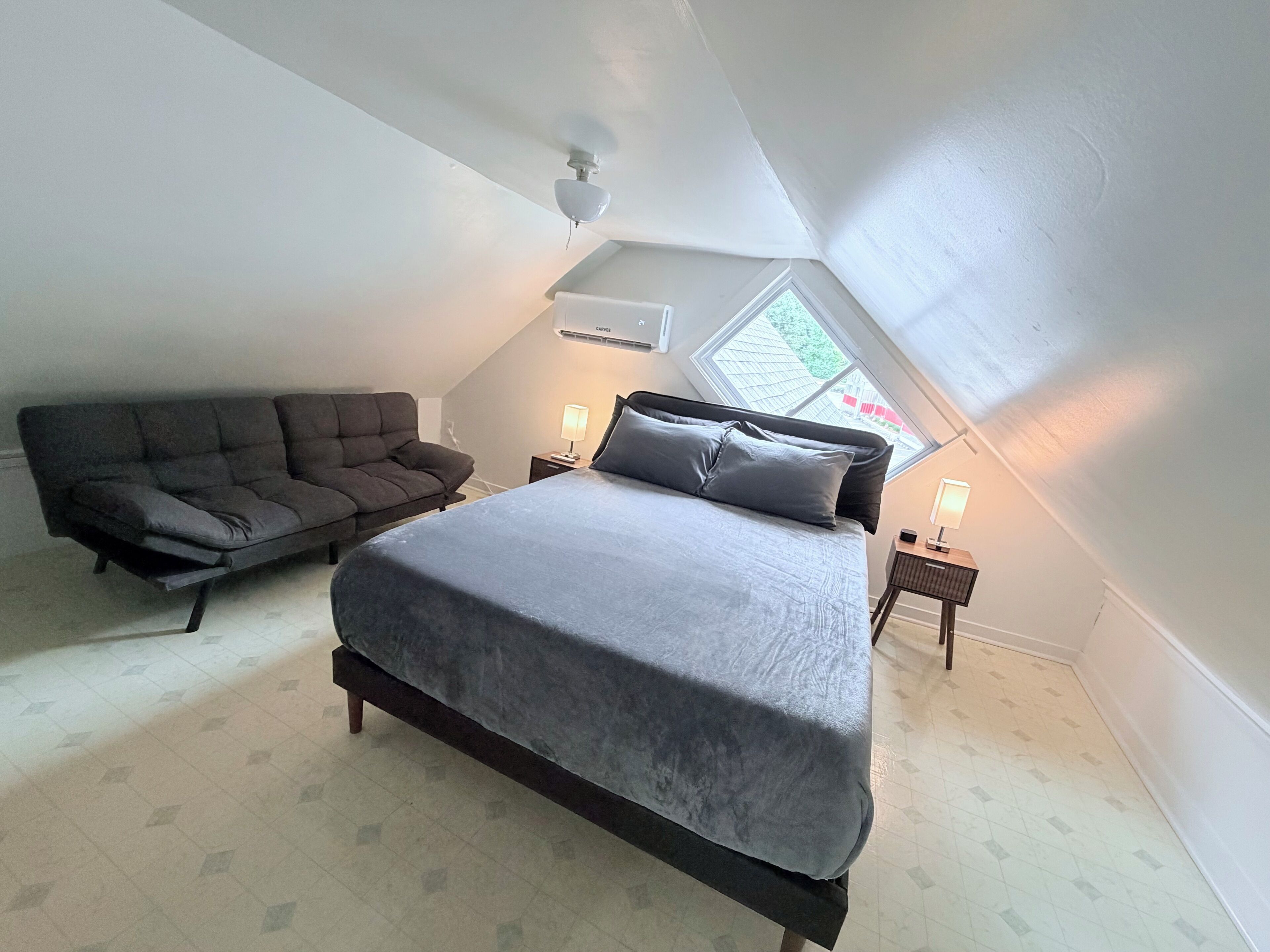 A bedroom with a bed, a sofa, two bedside tables, and a skylight.