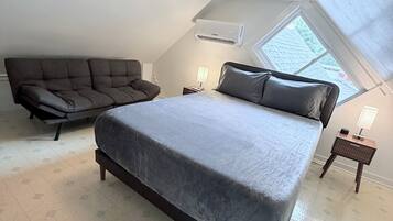 A bedroom with a large bed, a sofa, a nightstand with a lamp, and a skylight.