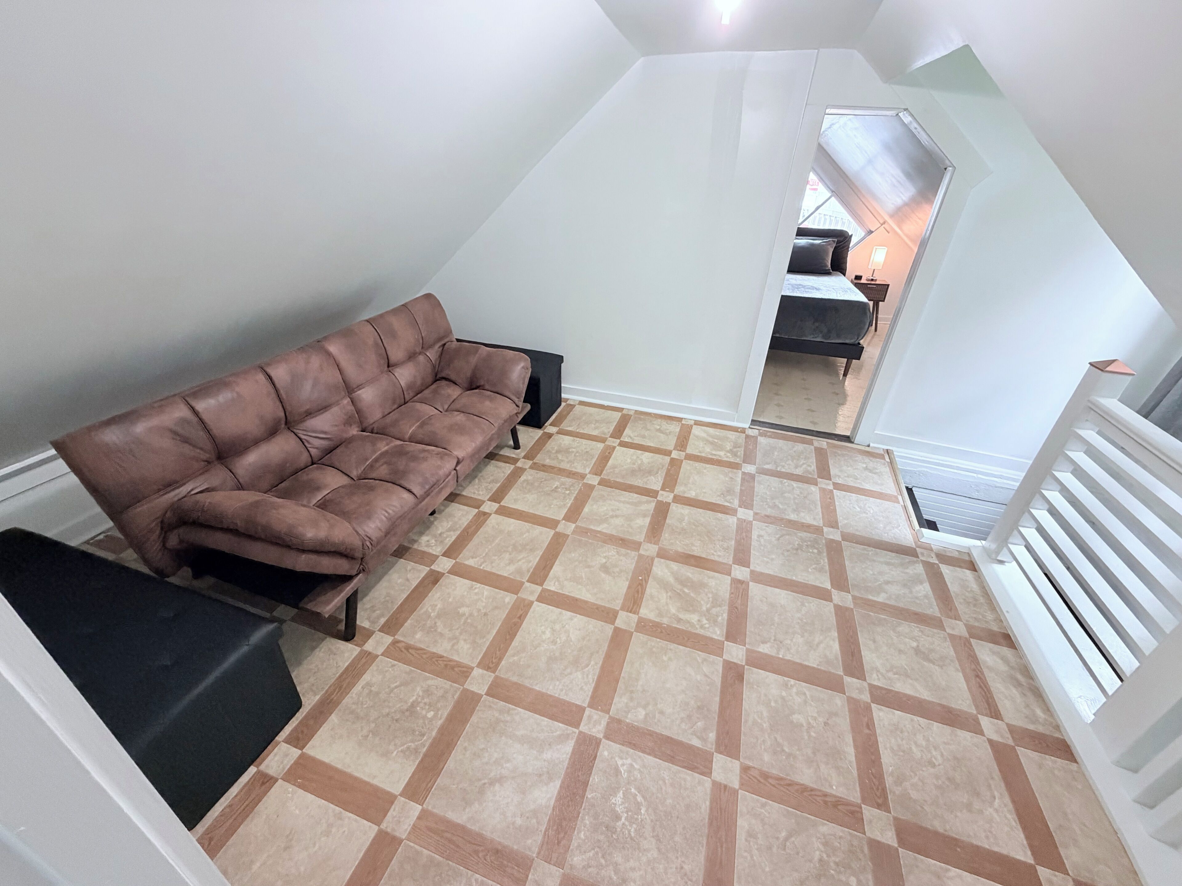 A loft-style room with a brown leather sofa, a patterned floor, and a white railing.