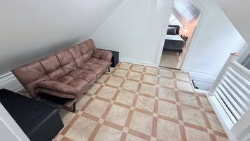 A loft-style room with a brown leather sofa, a patterned floor, and a white railing.