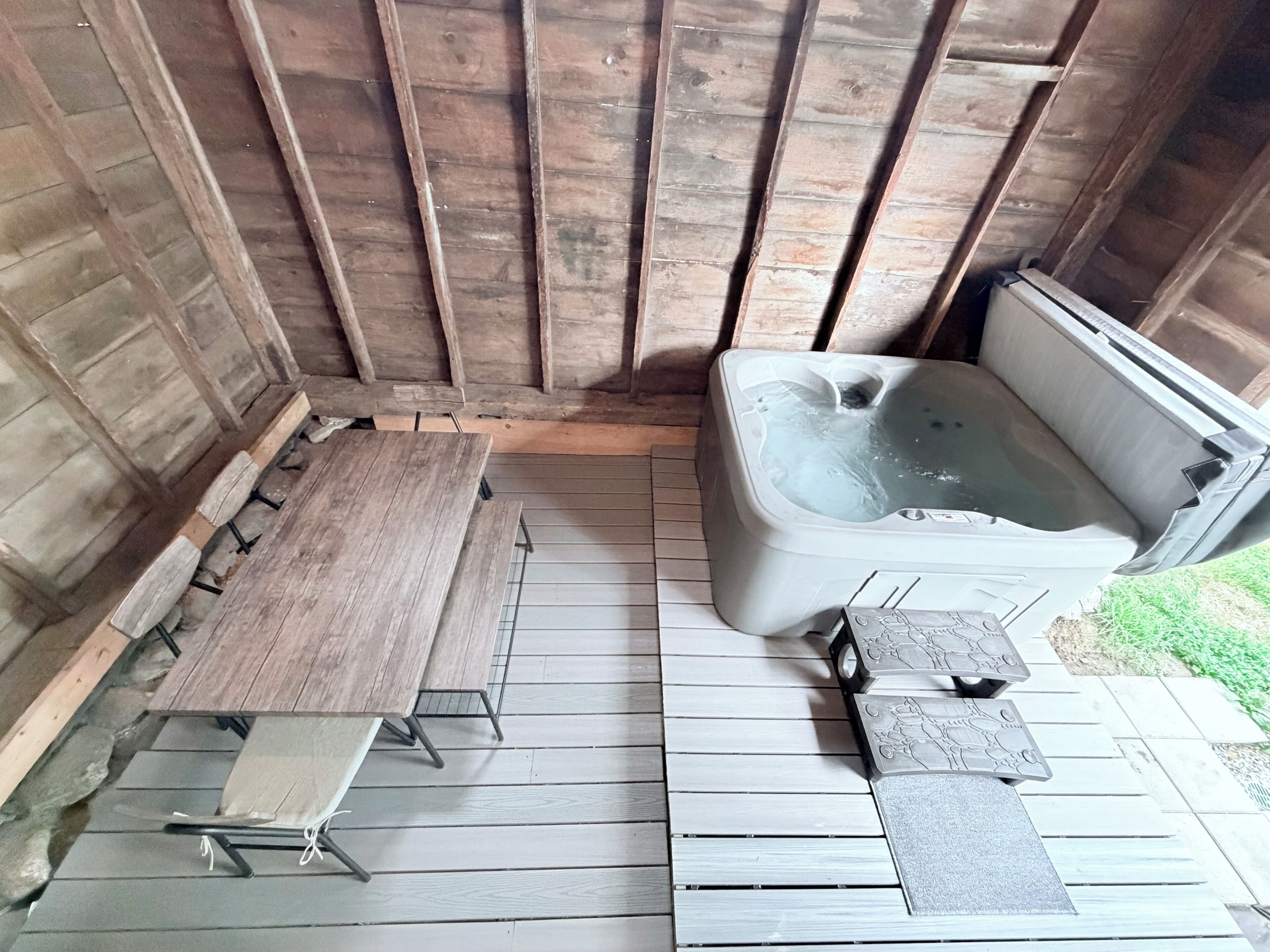 A wooden deck with a hot tub, a table, and benches.