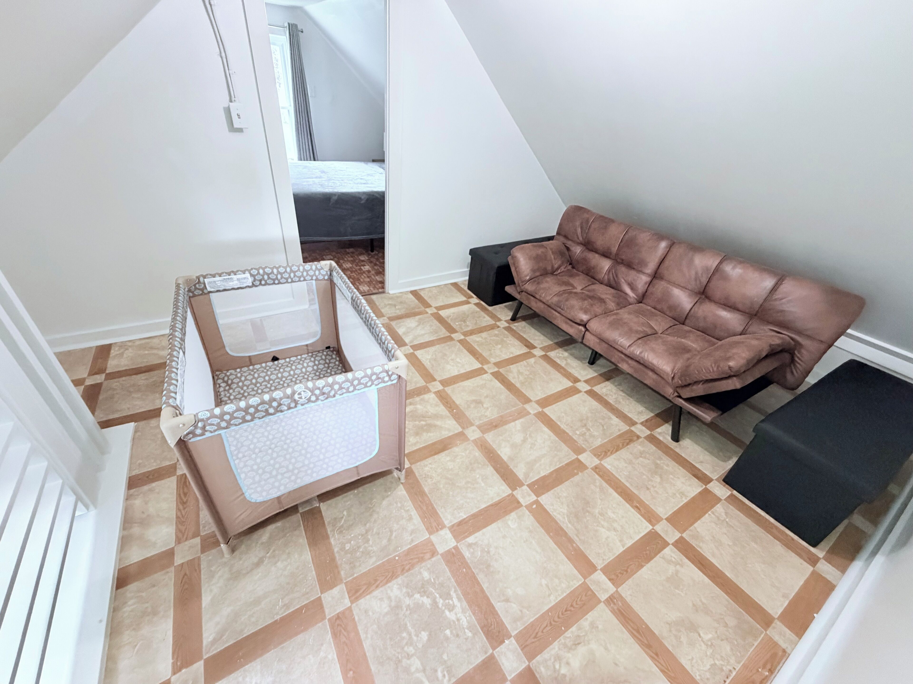 Une pièce avec un sol à carreaux, un canapé en cuir marron, une armoire blanche et un banc noir.