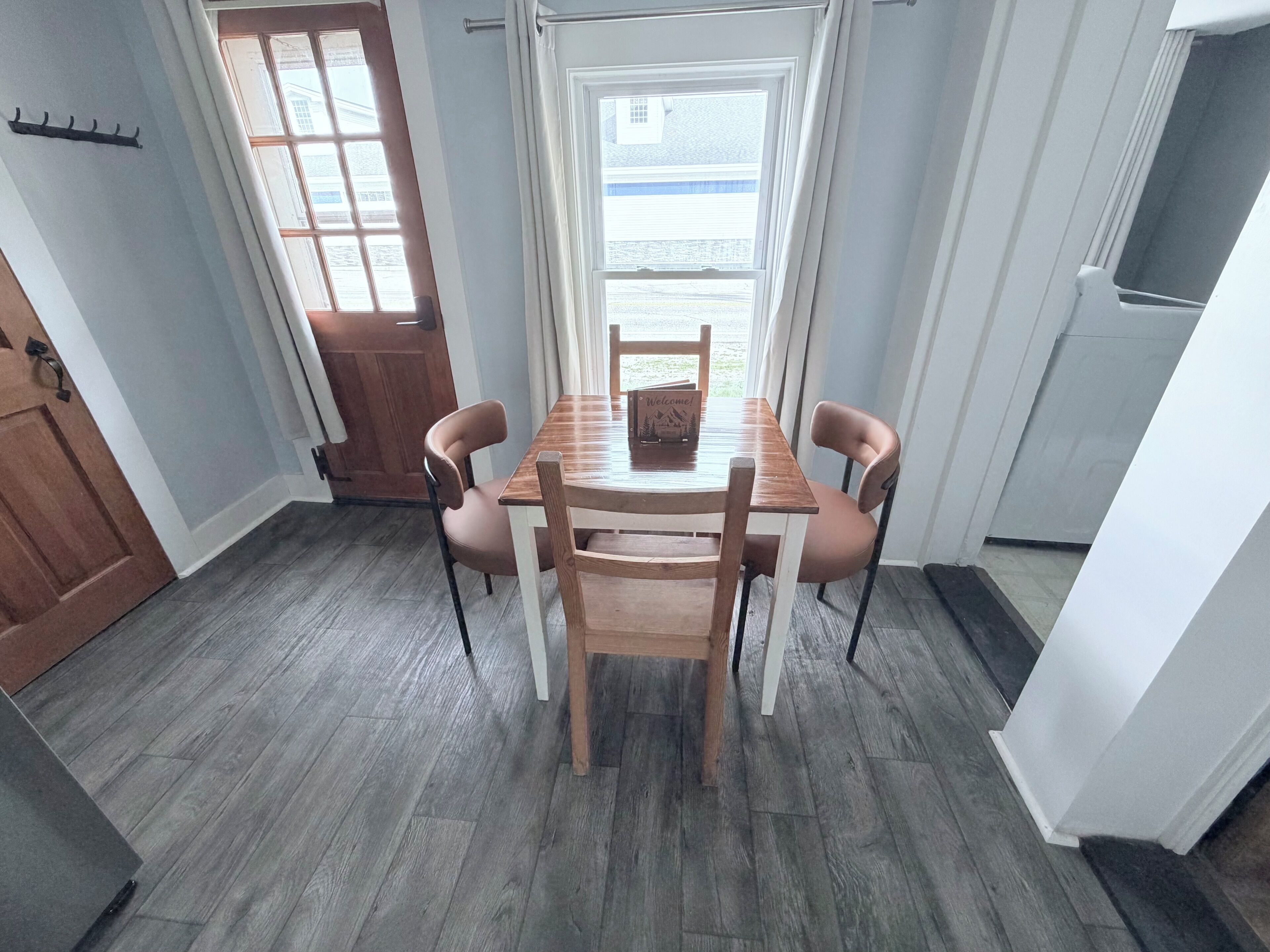 A dining area with a wooden table and chairs, a window with curtains, and a door.
