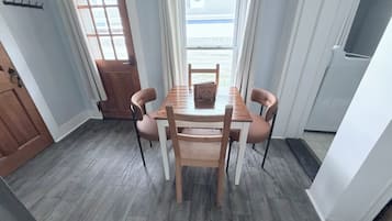A dining area with a wooden table and chairs, a window with curtains, and a door.