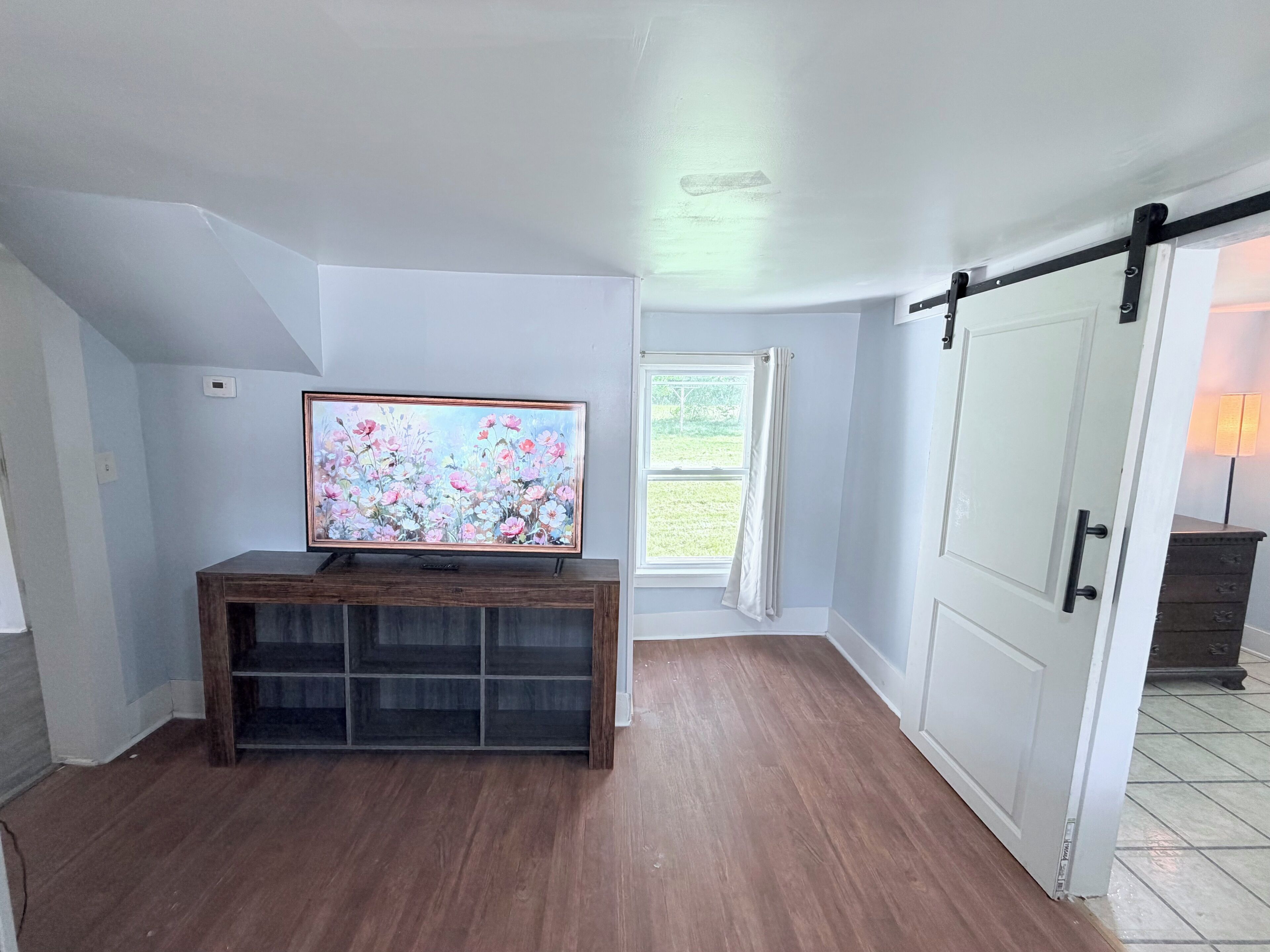 A room with a wooden entertainment center, a large painting, a window with curtains, and a sliding door.