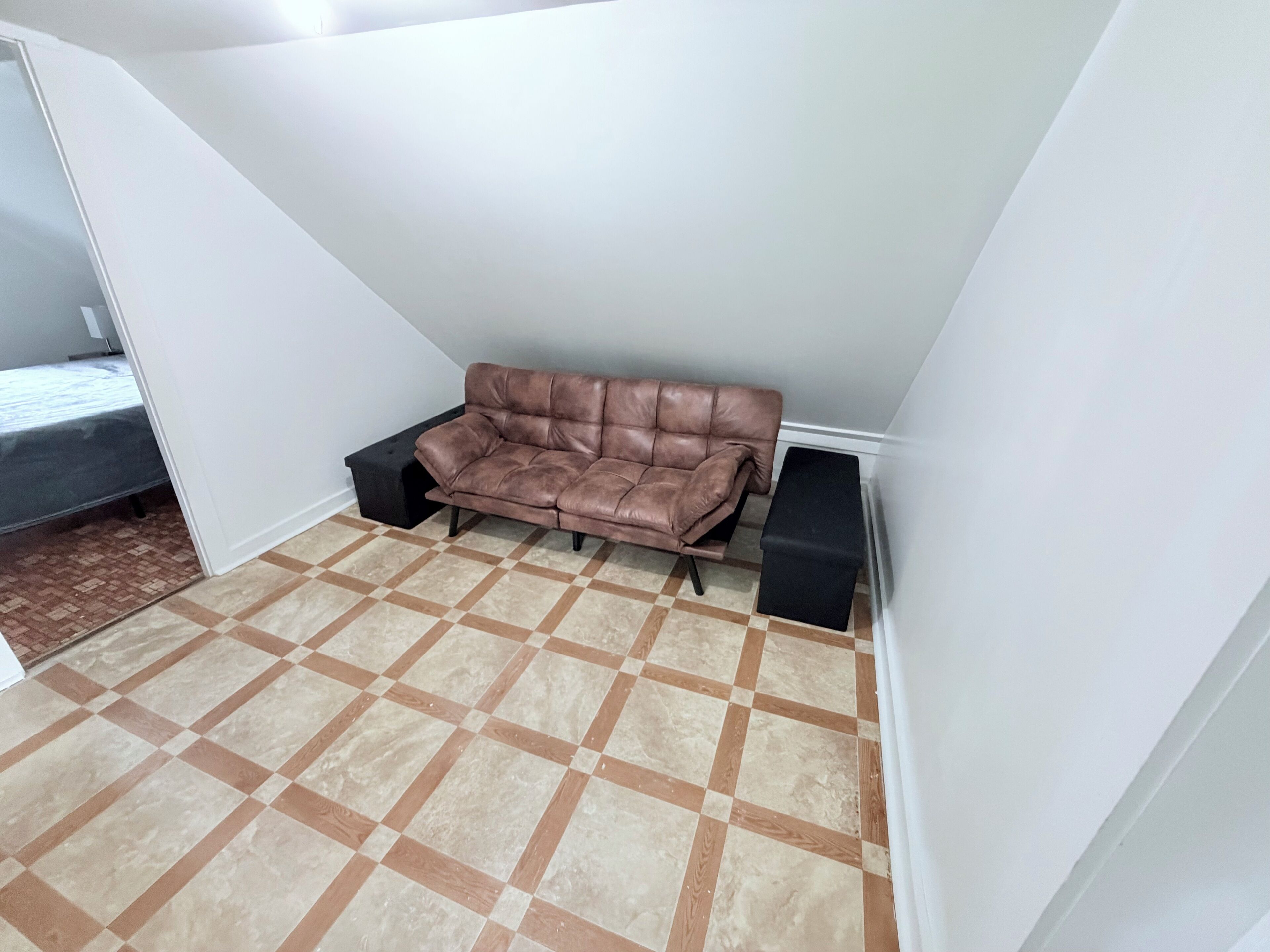 A room with a brown leather sofa, two black ottomans, and a checkered floor.
