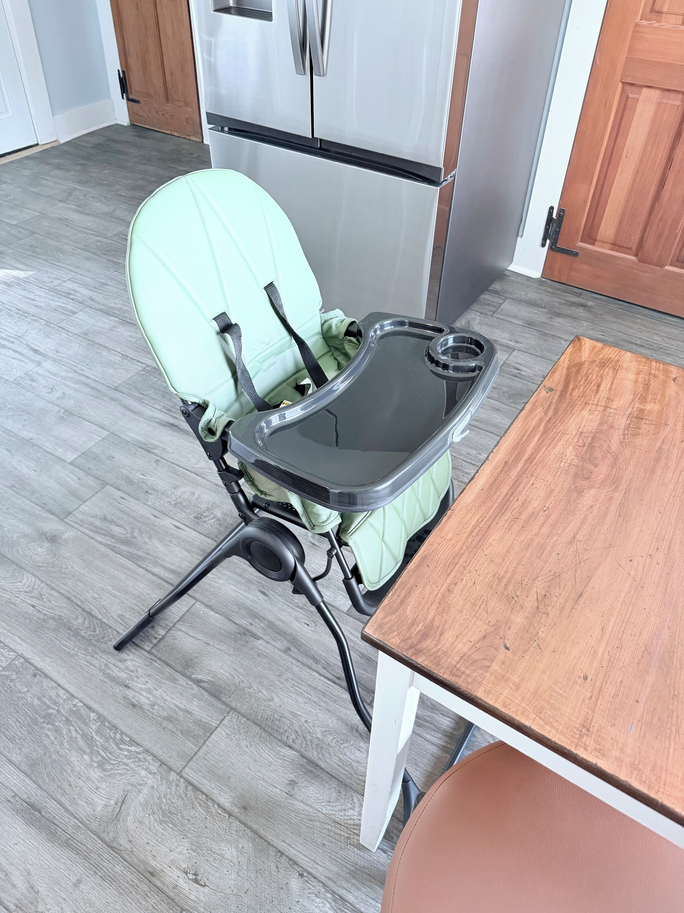 A compact kitchenette with a modern refrigerator, a small table, and a chair with a tray.