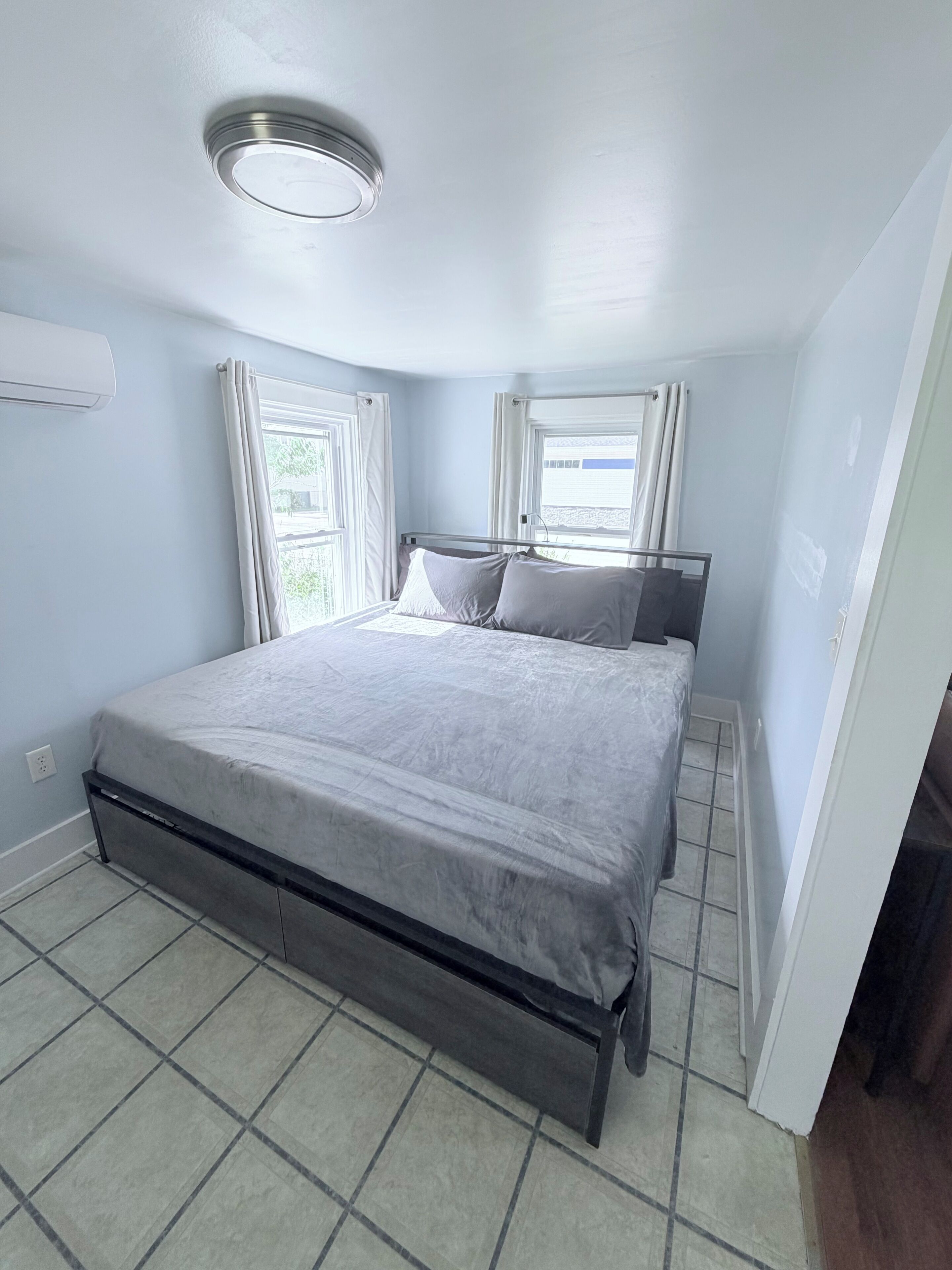 A bedroom with a bed, a ceiling light, and a window with curtains.