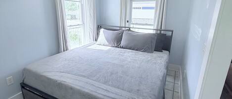 Un dormitorio con una cama, una lámpara de techo y un ventanal con cortinas.