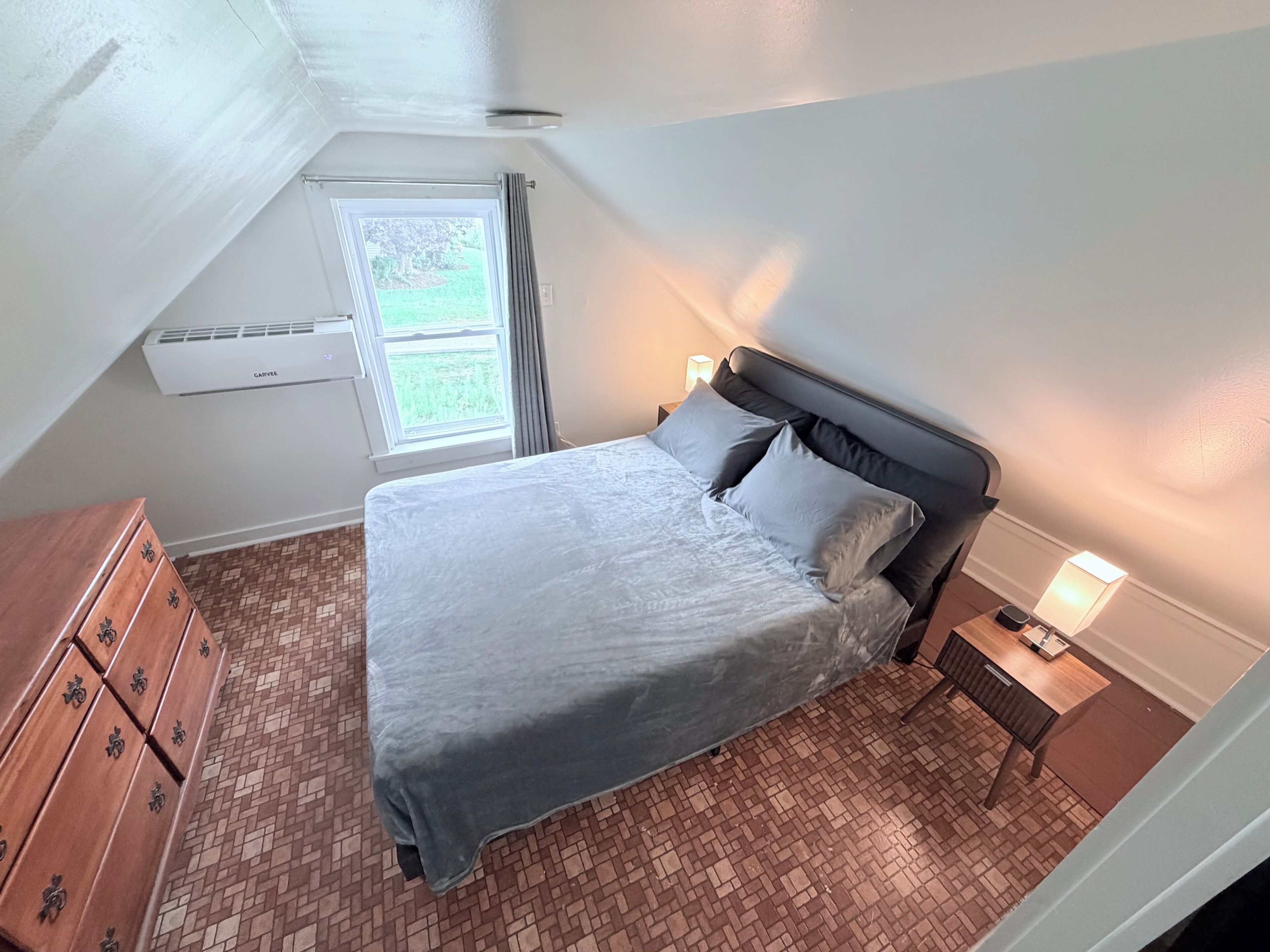 Un dormitorio con cama, cómoda, mesita de noche y ventana con cortinas.