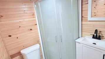 A compact bathroom with a toilet, a glass-enclosed shower, and a sink with a mirror above it.