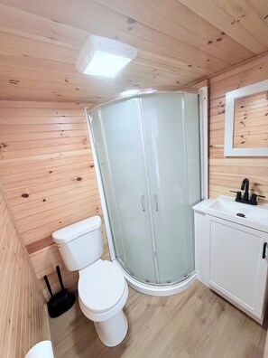 Een kleine badkamer met toilet, een douche met glazen wand en een wastafel met spiegel erboven.