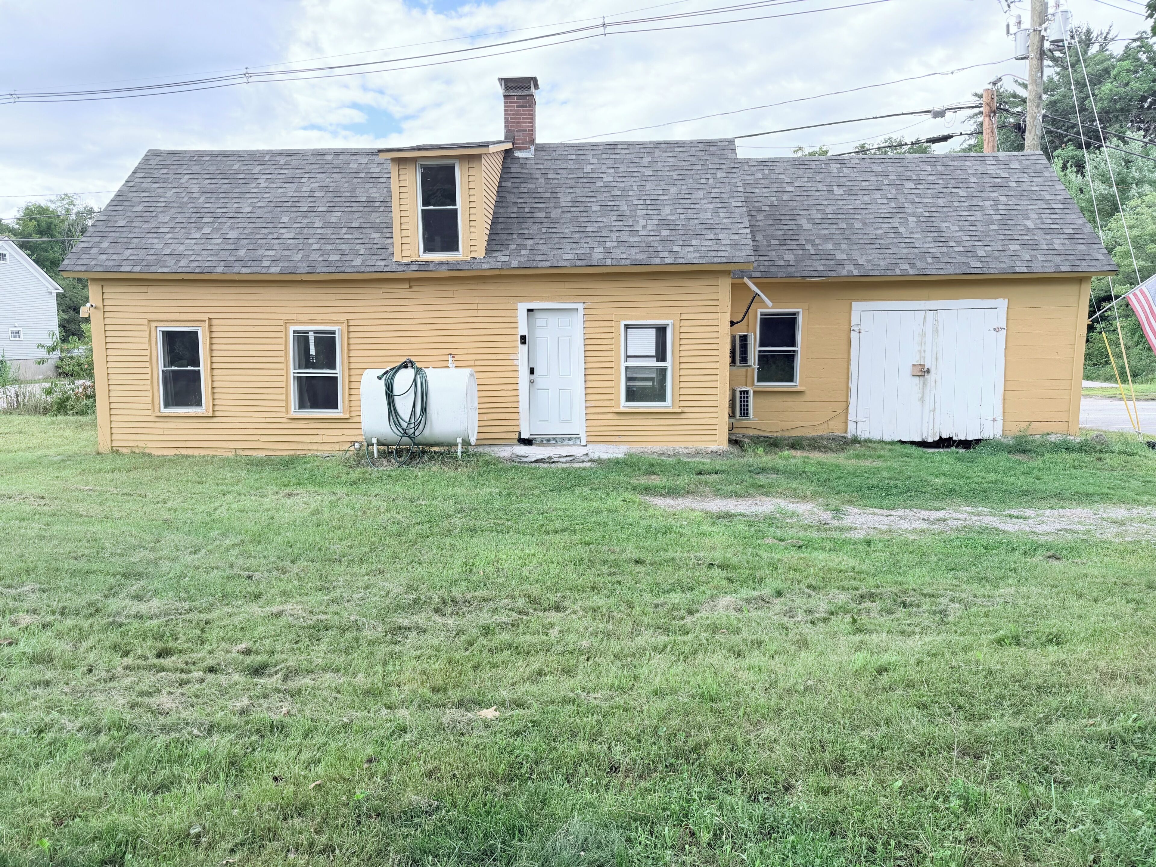 A single-story yellow house with a grey roof, a front door, and a small attached garage.