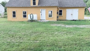 Une maison jaune à un seul étage, avec un toit gris, une porte d’entrée et un petit garage attenant.