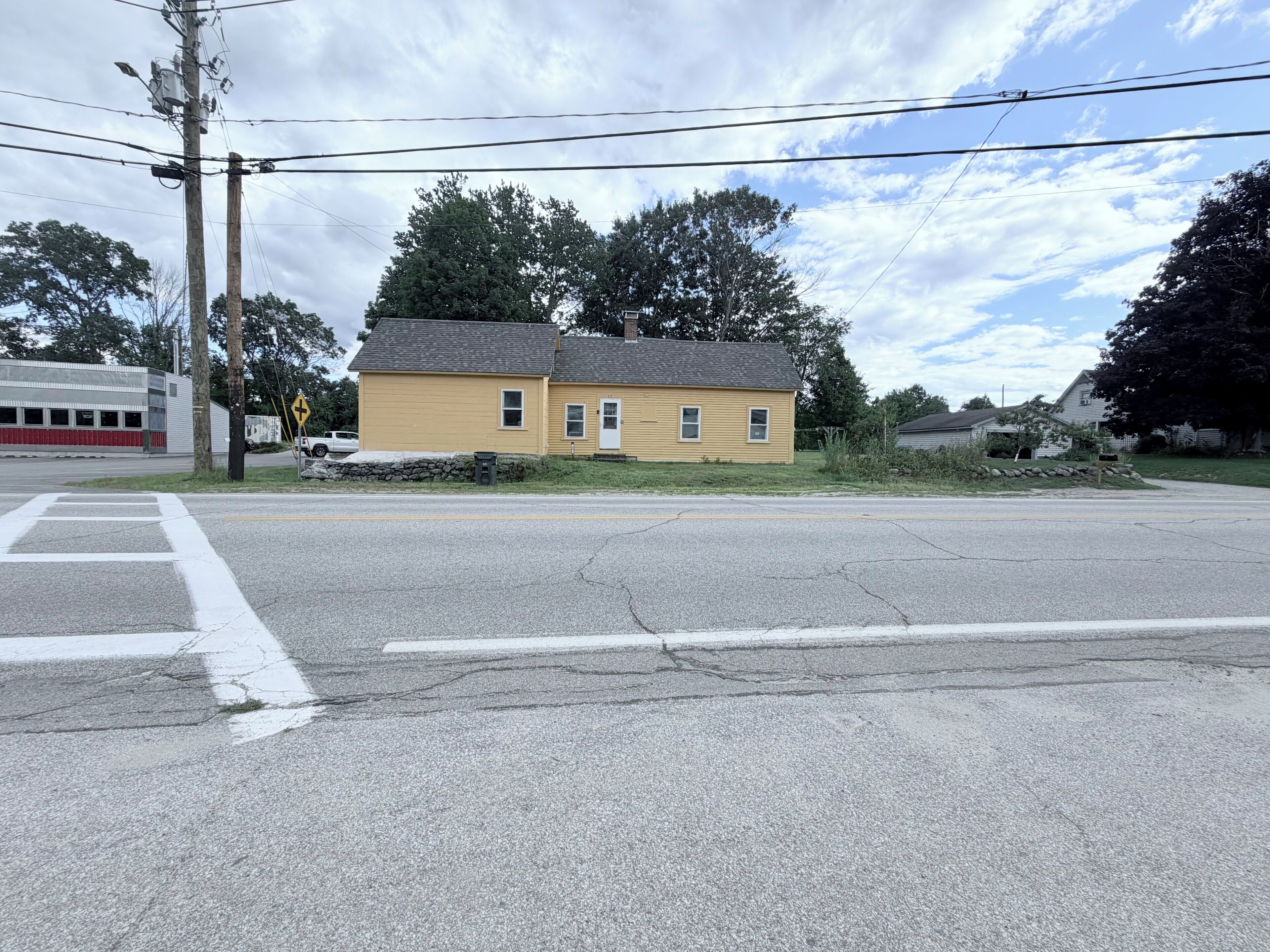 A two-story yellow house with a garage, located at a street intersection with a crosswalk.