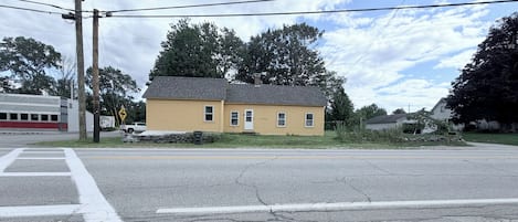 A two-story yellow house with a garage, located at a street intersection with a crosswalk.