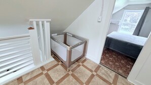 Une pièce avec un plafond en pente, un berceau, un lit et une fenêtre avec des rideaux.