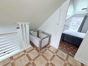 Een kamer met een schuine kap, een kinderbedje, een bed en een raam met gordijnen.