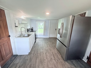 A modern kitchen with white cabinetry, stainless steel appliances, and a wooden floor.