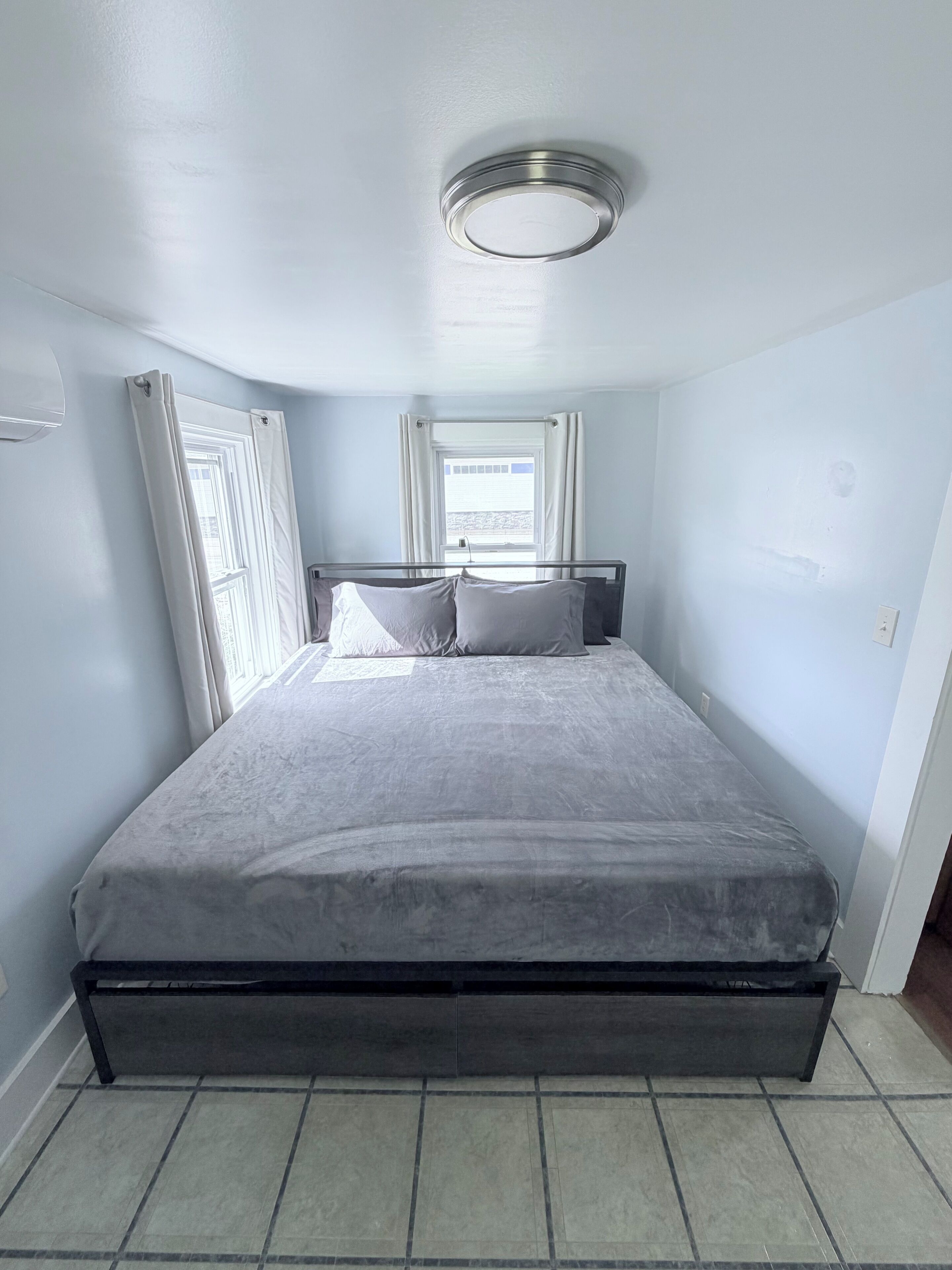 A bedroom with a bed, a window with curtains, and a ceiling light fixture.