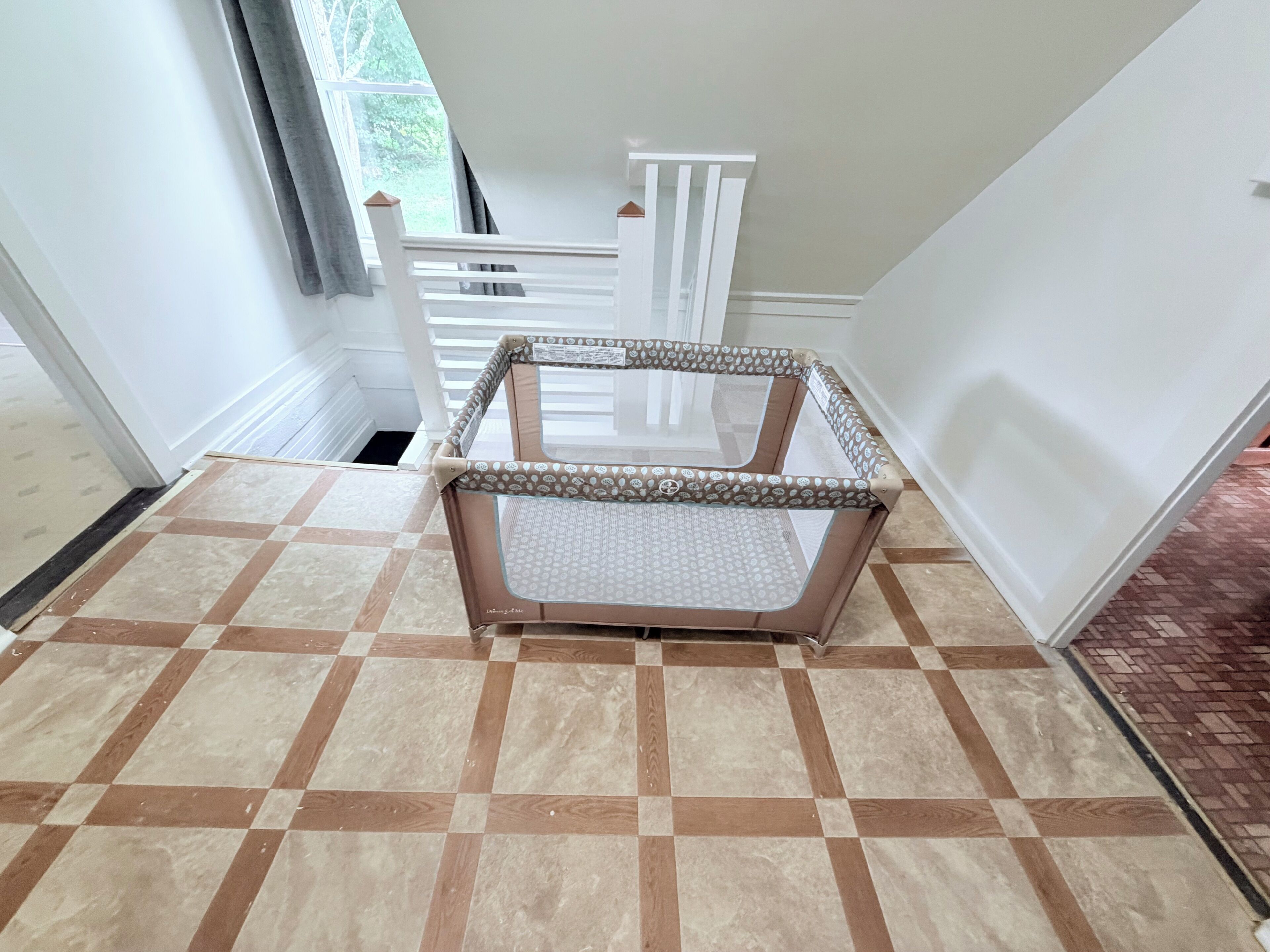 Une pièce avec un sol à carreaux, une rambarde blanche et une fenêtre avec des rideaux.