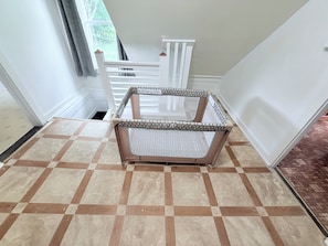 Une pièce avec un sol à carreaux, une rambarde blanche et une fenêtre avec des rideaux.