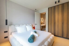 A modern bedroom with a large bed, a wooden wardrobe, and a bathroom visible through an open door. - Azure at The Reef Superior | Ocean View Penthouse (Willemstad)