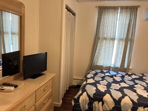 A bedroom with a bed, a television on a dresser, a window with curtains, and a wooden floor. - Lovely 1-bedroom condo with pool in lovely Wildwood right by beach and boardwalk (Wildwood)