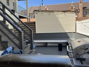 Um terraço no telhado com churrasqueira, área de estar ao ar livre e escada que dá acesso a um andar superior.
