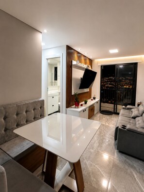 Ein modernes Wohnzimmer mit einer Couch, einem Esstisch und einer Küchenzeile mit Fernseher.