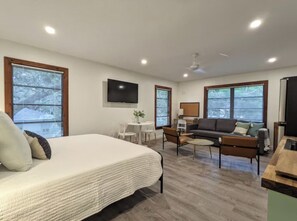 A modern bedroom with a large bed, a desk, a sofa, and a TV mounted on the wall. - Updated Old Florida Studio Apartment Getaway in Central Sarasota (Sarasota)
