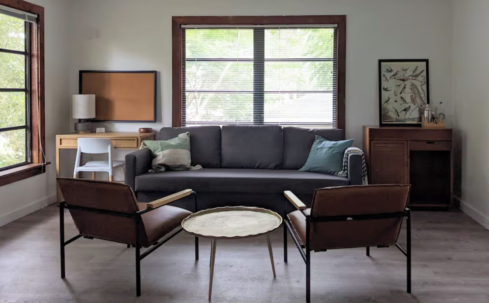 A living room with a sofa, two armchairs, a coffee table, a desk with a lamp, and a painting on the wall.