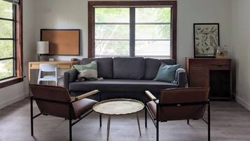 A living room with a sofa, two armchairs, a coffee table, a desk with a lamp, and a painting on the wall.