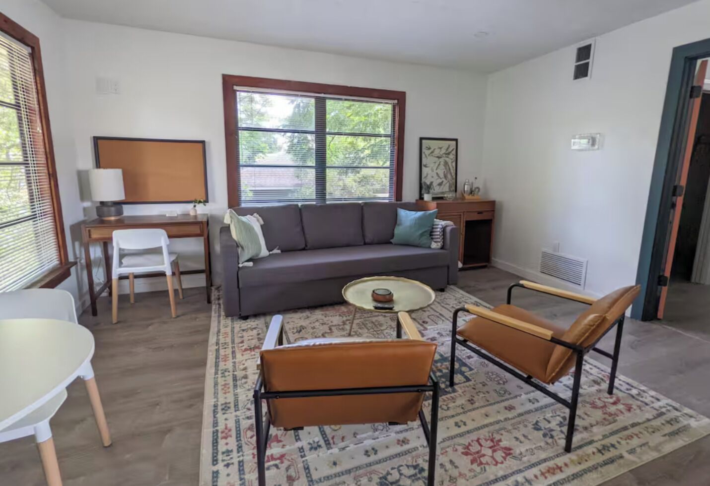 A living room with a sofa, two chairs, a coffee table, a desk, and a window with blinds.