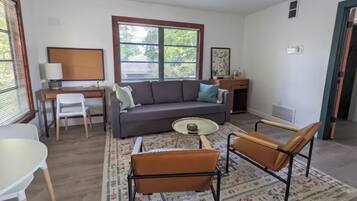 A living room with a sofa, two chairs, a coffee table, a desk, and a window with blinds.