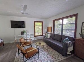 A living room with a sofa, chairs, a coffee table, a TV, and windows with blinds. - Updated Old Florida Studio Apartment Getaway in Central Sarasota (Sarasota)