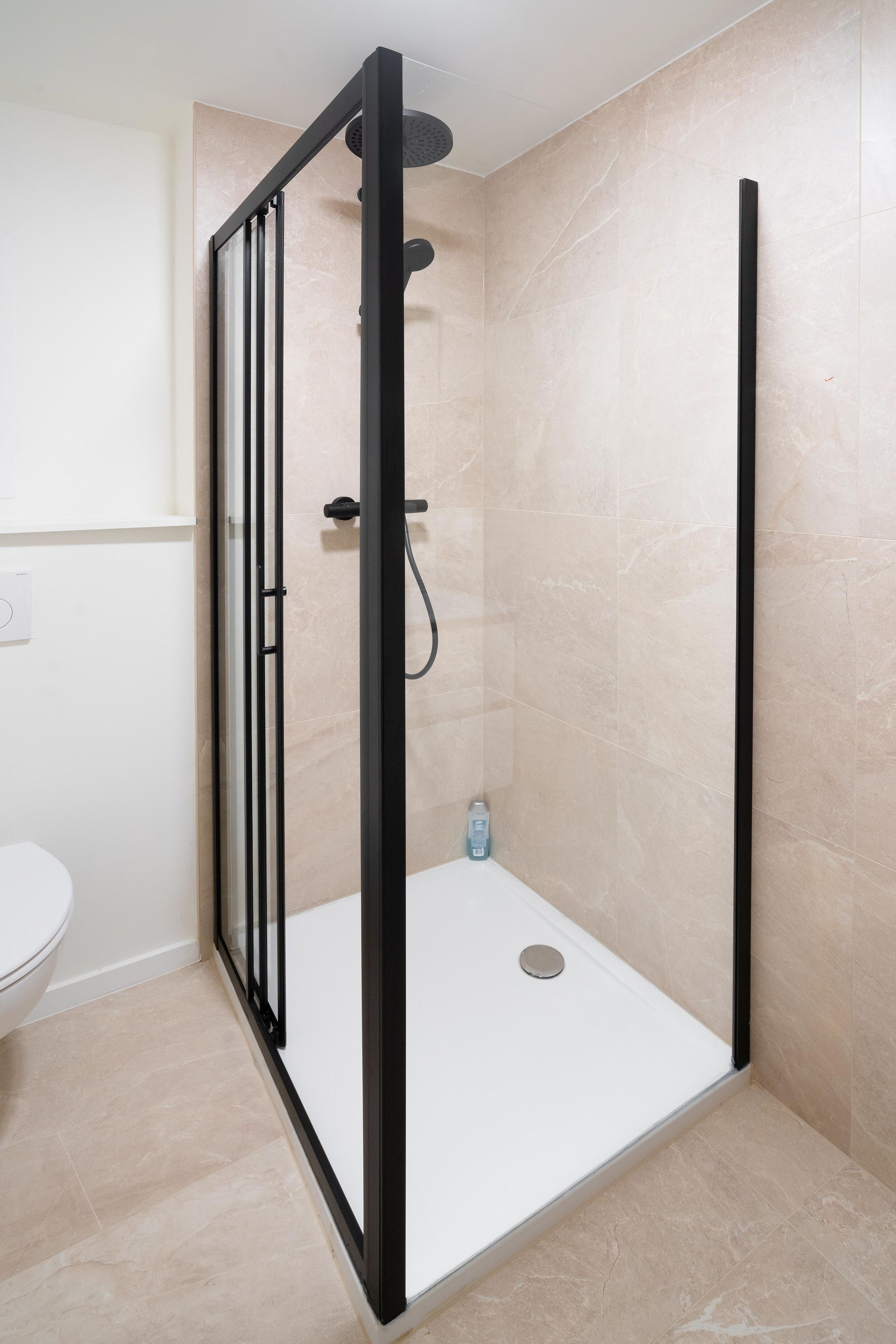 A modern bathroom with a glass-enclosed shower, a white toilet, and beige tiled walls.