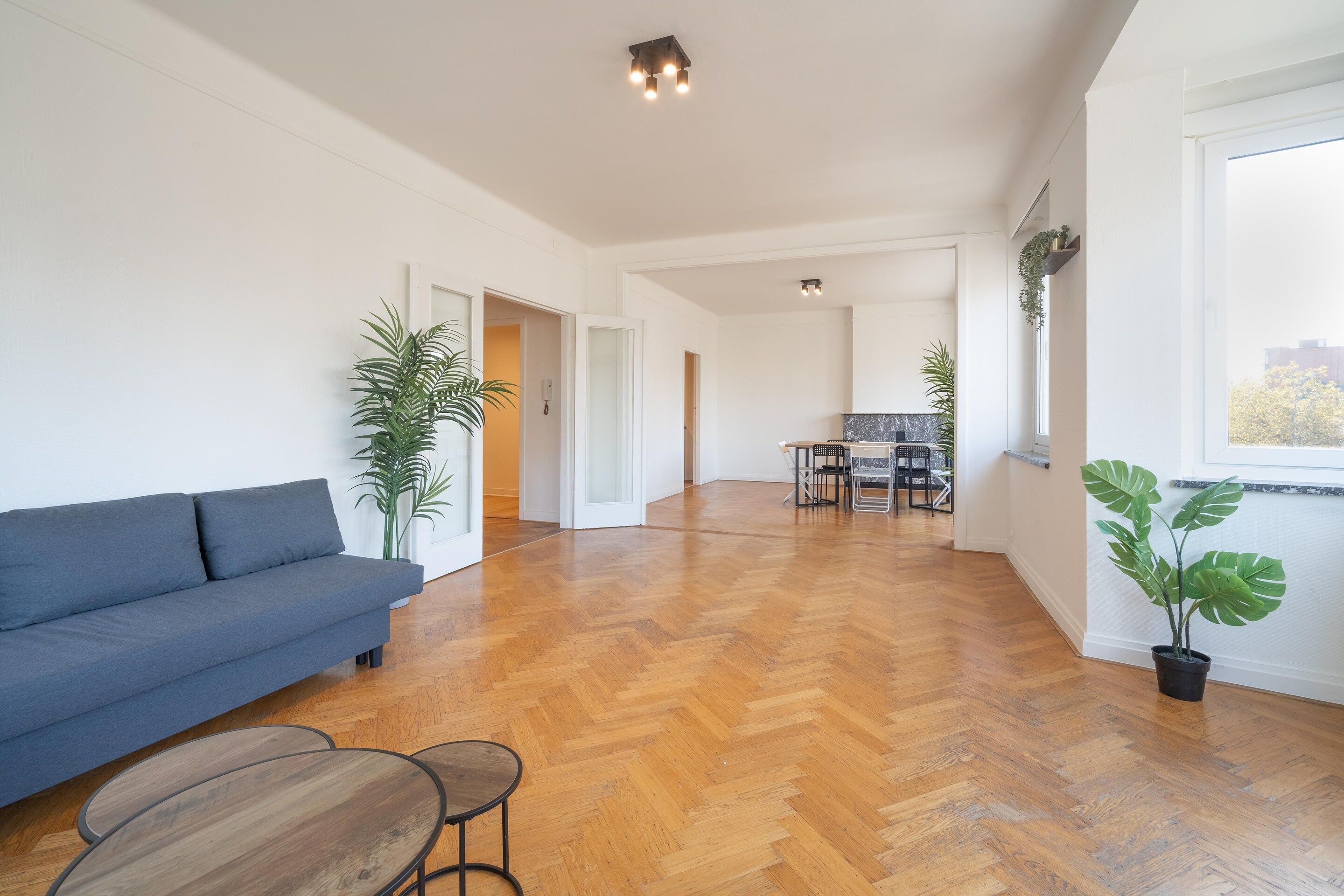 Un vaste espace de vie comprenant un canapé, une table à manger et des chaises, une cuisine à l’arrière-plan et de grandes fenêtres.